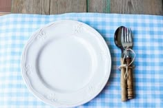 a white plate and silverware on a blue checkered table cloth