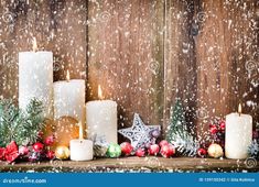 candles and christmas decorations on a wooden table with snow falling over the wood wall behind them