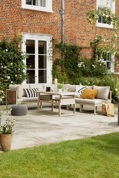 an outdoor living area with furniture and flowers in the foreground, next to a brick building