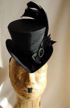 This gothic victorian mini top hat is an excellent choice for any dark cabaret event. It is covered with taffeta and embellished with various black trimmings. Two curled black rooster feathers, ribbons, a silver and black rhinestone round buckle and a just a hint of black veil. Choose between total black(pictured),blue or burgundy with black decoration. Measurements : height 4 inches( 10 cm ) front to back 9 inches ( 22 cm ) side to side 7.5 inches ( 19 cm ) This mini top hat is fully lined with Black Top Hat For Costume, Gothic Black Mini Hats For Halloween, Black Fitted Top Hat For Costume, Fitted Black Top Hat For Costume, High Crown Top Hat For Carnival Costume, Gothic Black Top Hat For Costume Party, Carnival Costume Top Hat With High Crown, Black Gothic Top Hat For Costume Party, Black Gothic Mini Hat With Adjustable Fit