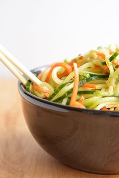 a wooden bowl filled with vegetables and chopsticks on top of a wood table