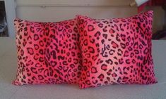 two pink and black leopard print pillows sitting on top of a white bedding set