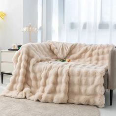 a couch covered in a fluffy blanket next to a table with a lamp on it