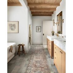 a long hallway with wood ceilinging and white walls, leading to a large bathroom