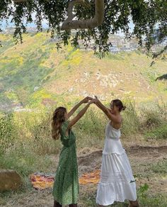 two women in dresses are holding hands under a tree