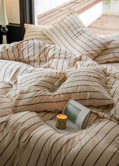 a book is laying on a bed with striped sheets and pillows, next to a lit candle