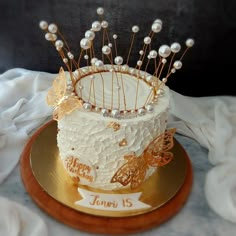 a white cake decorated with pearls and butterflies on a gold plated serving platter