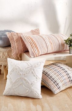 four pillows are arranged on a bench in front of a white wall and wooden floor