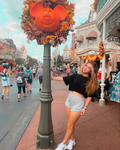 a woman standing next to a pole with a giant pumpkin on it's head