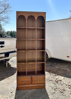 a large bookcase sitting in the middle of a parking lot next to a white truck