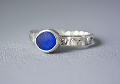 a silver ring with a blue stone in the center on a white surface, close up