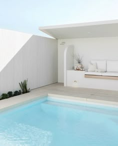 an empty swimming pool in front of a white building with a couch on the side