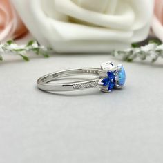 This beautiful ring is made from genuine 925 sterling silver with rhodium plating. Ring details- -The Main stone is a round cut 6mm Lab Created Light Blue Opal Stone -Side stones are 4mm by 2mm Lab Blue Sapphire Marquise and 1mm Round simulated diamonds -Ring is casted in solid 925 sterling silver with rhodium plating (yellow gold and rose gold plated also available, please check the drop down menu for more options) -The Total face height of the ring measures 7mms and the band width measures 1.5 Blue Sterling Silver Open Ring, Blue Three Stone Sapphire Ring In Sterling Silver, Blue Gemstone Cluster Ring For Anniversary, Blue Cubic Zirconia Birthstone Promise Ring, Blue Birthstone Cluster Ring For Anniversary, Blue Birthstone Ring With Accent Stones For Anniversary, Blue Cluster Ring With Prong Setting For Promise, Blue Hallmarked Opal Ring For Wedding, Blue Topaz Three Stone Blue Jewelry