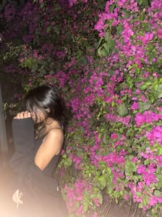 a woman standing in front of purple flowers at night with her hand on her face