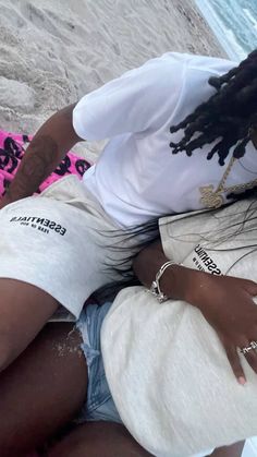 a woman laying on top of a beach next to the ocean with her hands in her pockets