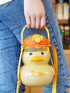 a person is holding a yellow duck shaped handbag in their right hand and wearing blue jeans