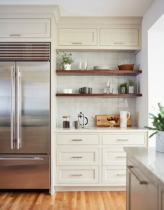 a stainless steel refrigerator in a white kitchen with open shelving and wooden flooring