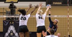 three women playing volleyball in front of the net with their hands up to block the ball