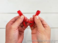 two hands are holding red ribbon in the shape of a heart on a white background