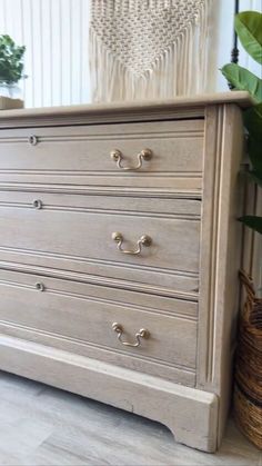 an old dresser is painted white and has gold knobs on the drawers, along with a plant in a wicker basket