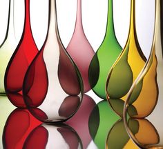 four different colored vases sitting next to each other on a reflective surface with reflections