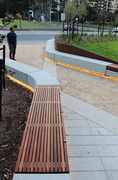 a wooden bench sitting on the side of a road next to a lush green park