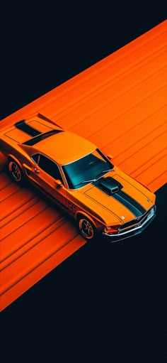 an orange and black car is parked on the side of a road in front of a red wall