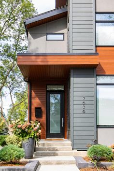 the front entrance of a modern home with wood siding and stone steps leading up to it