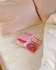 a pink book laying on top of a bed next to two white pillows and blankets