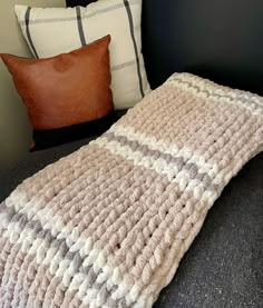 a crocheted blanket sitting on top of a couch next to two brown pillows