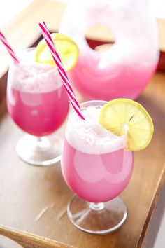 two glasses filled with pink lemonade and topped with straws on a wooden tray