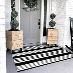 two planters are on the front porch with black and white striped rug in front