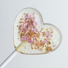 a heart shaped lollipop with pink and gold sprinkles on it