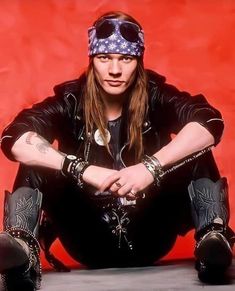 a man sitting on the ground with his legs crossed and wearing sunglasses, leather jacket and bandana