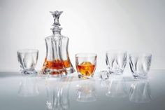 an assortment of liquor glasses and decanter on a reflective surface with white background