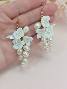 a pair of white flowers and pearls are hanging from gold - toned earwires