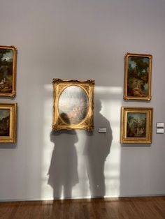 the shadow of a person standing in front of three paintings on a white wall with wooden floors