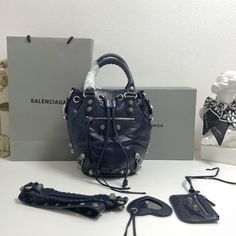 Balenciaga 's popular 'Le Cagole' series is a modern interpretation of its 'City' handbags - reshaped into a bucket bag design to inject a new soul into it. The large size adds two round top handles, combining classic and Modern trends are perfectly integrated. On the basis of retaining the original DNA of the motorcycle bag's flat rivets, delicate buckles and tassel zippers, it adds adjustable woven shoulder straps and a cute and playful heart-shaped mirror, which perfectly softens the neutral New Soul, Shaped Mirror, Motorcycle Bag, Lv Purse, Lv Shoes, Gucci Bamboo, Lv Handbags, Orange Bag, Round Top