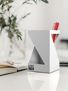 a desk with a book, pen and pencil holder on it next to a plant