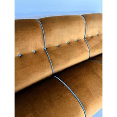 a brown couch with blue piping and buttons on the armrests, in front of a blue wall