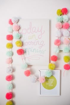 a white wall with pom - poms hanging from it's sides and a sign that says, simple garland