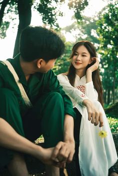 a young man and woman sitting next to each other in the woods, with trees behind them