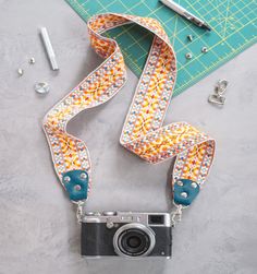 the camera strap is being used to hold an old camera and other items on a table