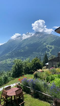 an outdoor table and chairs in front of a mountain range with flowers on the lawn