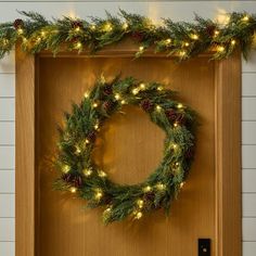 a christmas wreath is hung on the front door with pine cones and lights around it