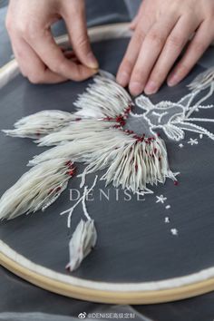 someone is working on an embroidery project with white feathers and red beads in the center