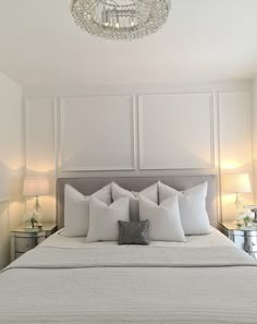 a bed with white sheets and pillows under a crystal chandelier