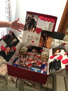 an open box filled with pictures and hearts on top of a table next to a person's hand