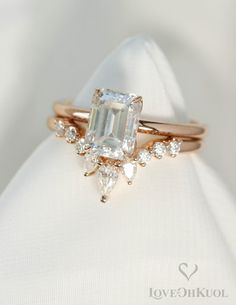 an engagement ring with a green emerald surrounded by small diamonds on top of a white cloth