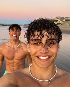 two men standing next to each other on the beach with their mouths open and smiling